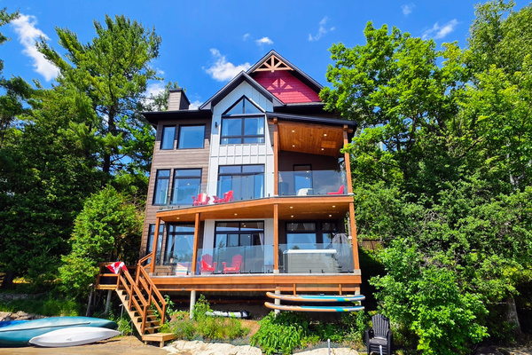 View of cottage from dock showing deck access, hot tub and watercraft stored at front of cottage