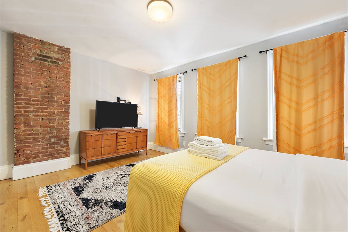 Comfortable queen-sized bedroom with a cozy workspace and TV — ideal for rest and productivity.
