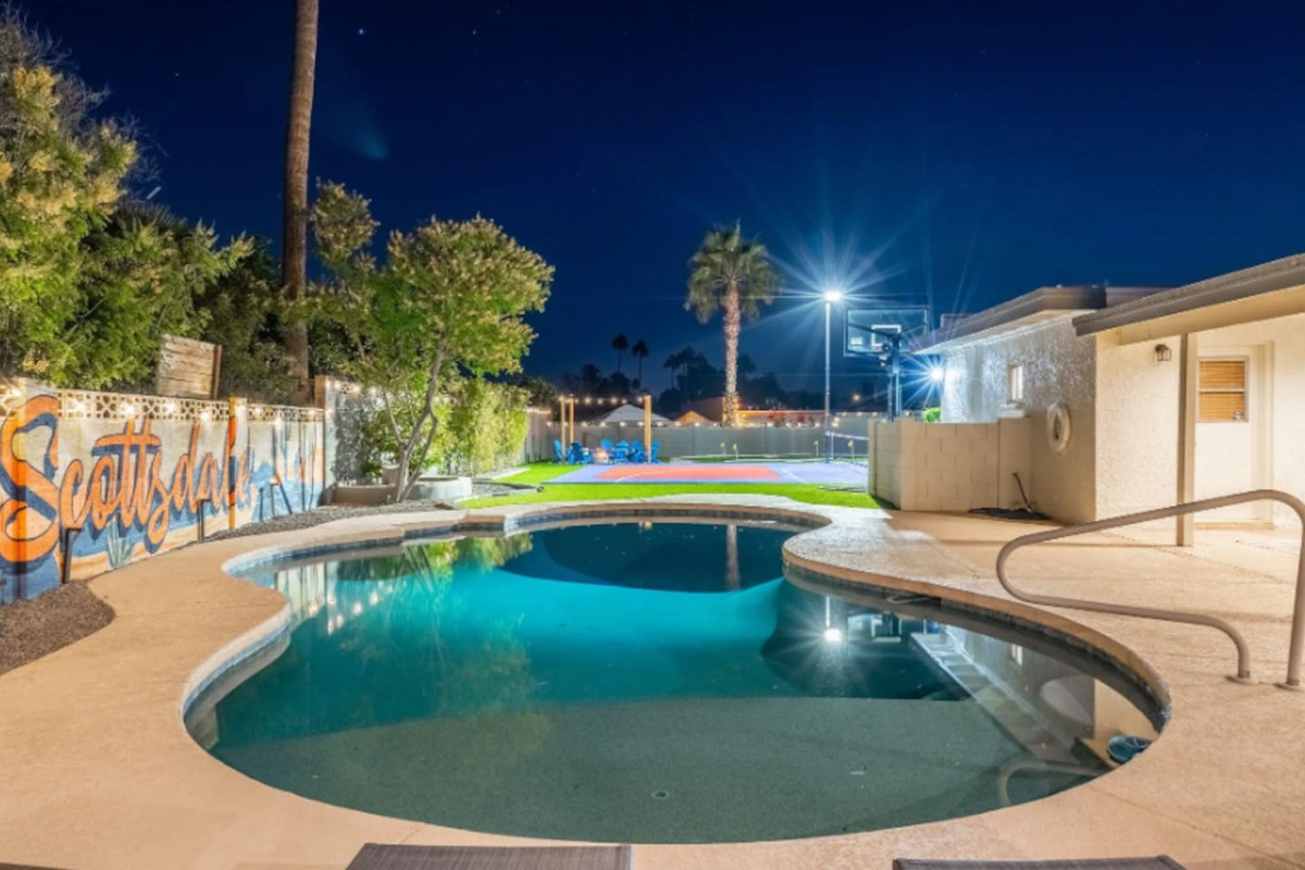 The pool glows at night, with the sport court lit just beyond — pick your pace, the whole backyard is yours.