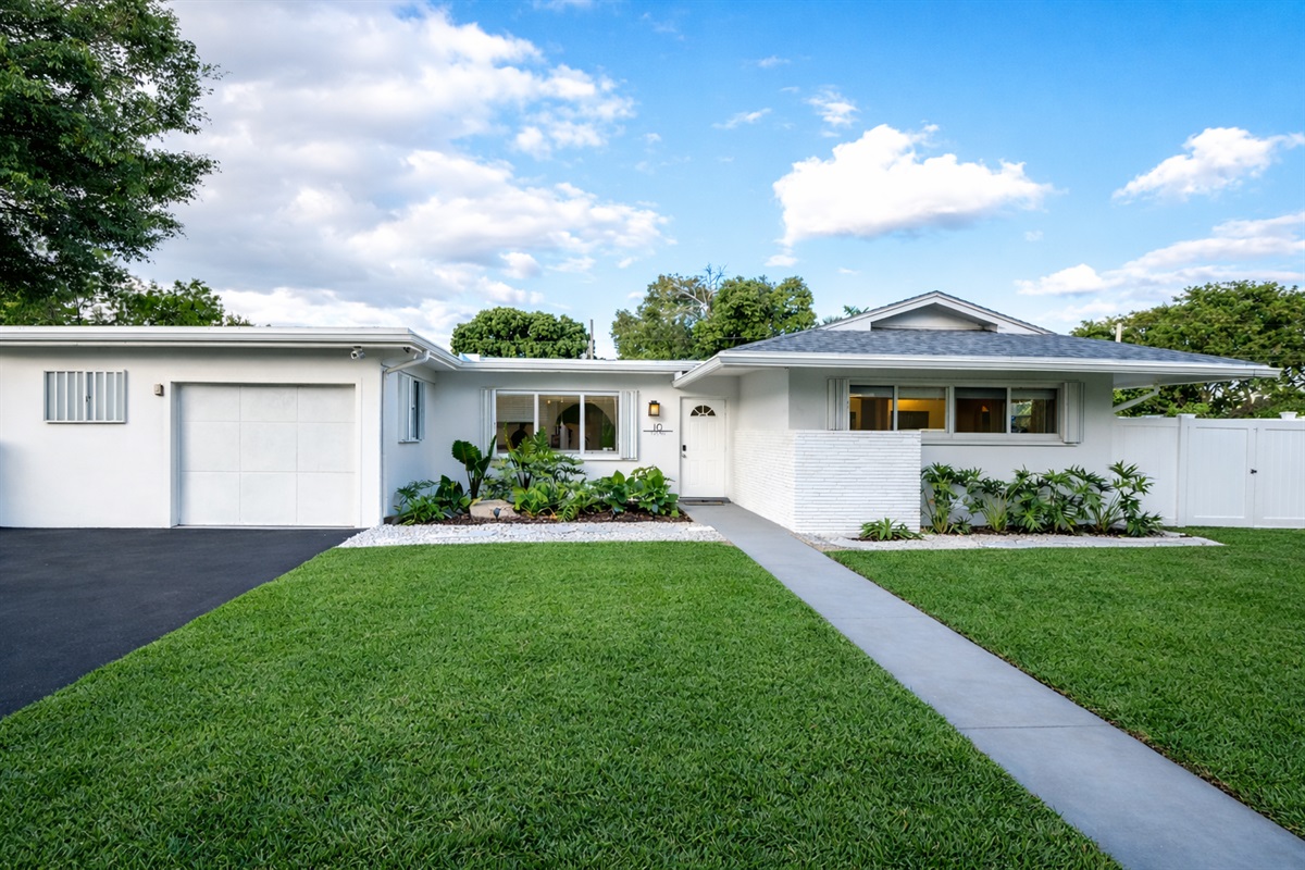 Crisp Palm Beach curb appeal with lush landscaping, private drive, and timeless mid-century charm in a quiet residential neighborhood.