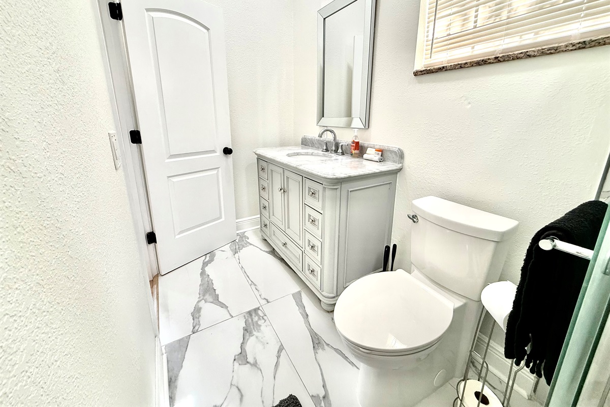 Crisp, clean, and contemporary, this full bathroom offers a polished look with a granite-style vanity, soft-close drawers, and a striking tile shower accented with glass and stone textures.