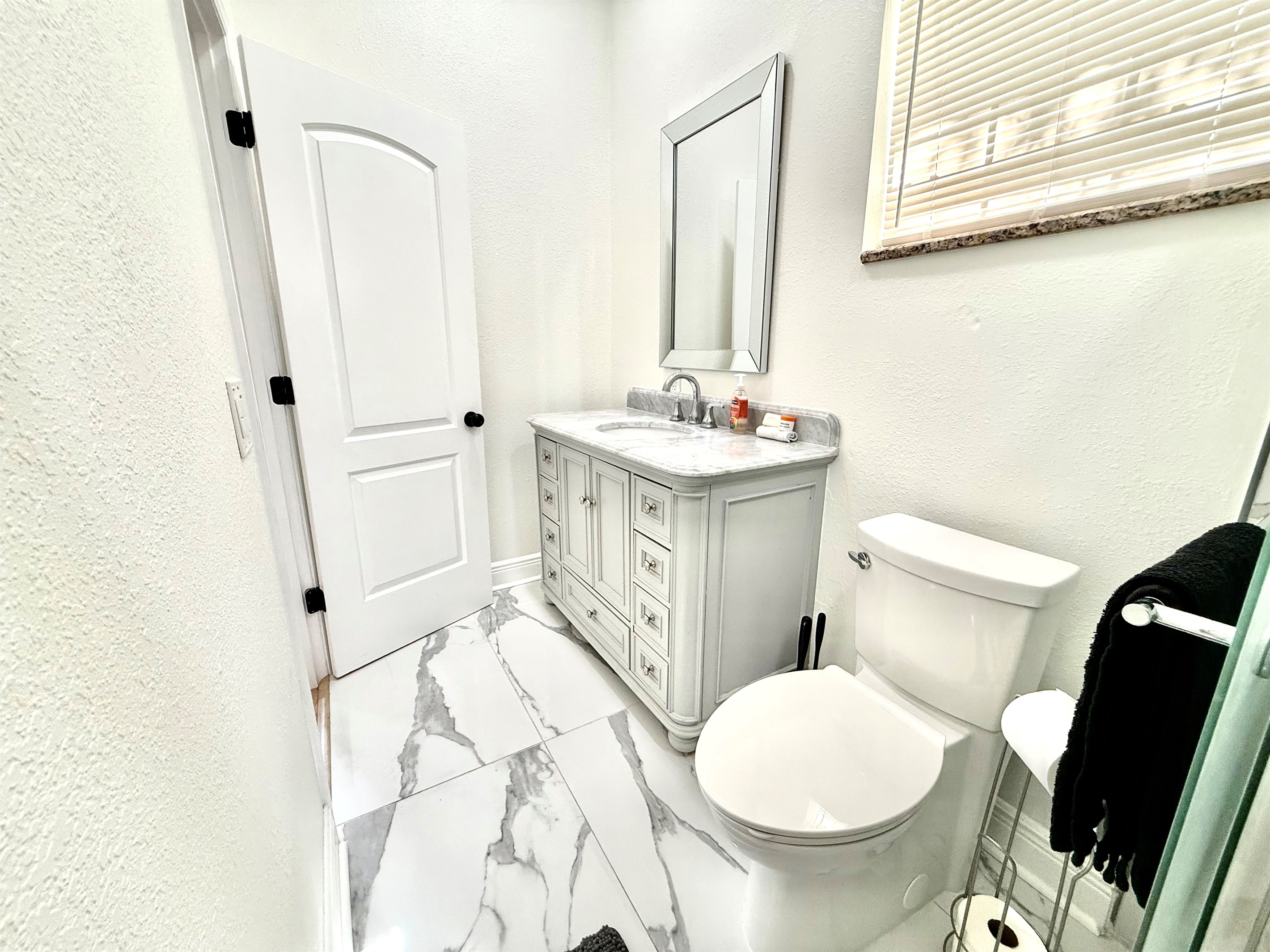 Crisp, clean, and contemporary, this full bathroom offers a polished look with a granite-style vanity, soft-close drawers, and a striking tile shower accented with glass and stone textures.