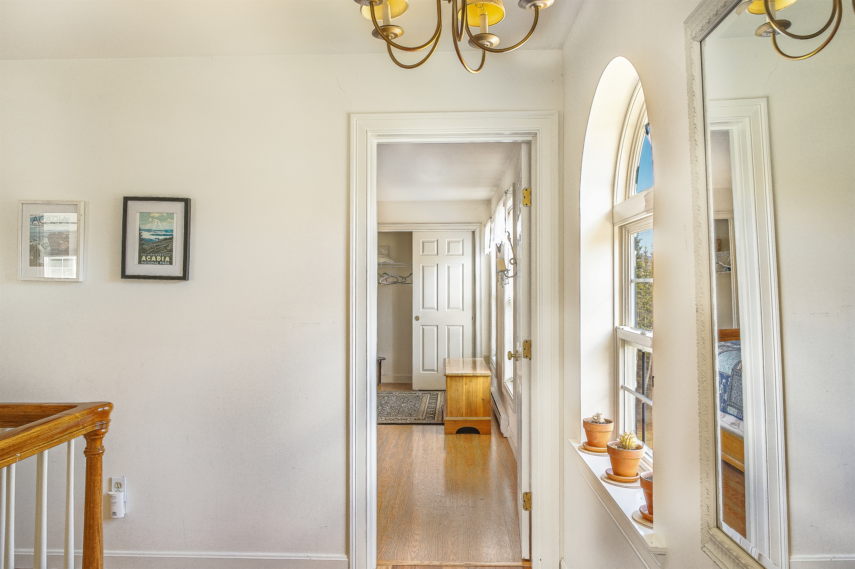 Experience the seamless flow from the twin room across the landing to the private Primary Suite. This sun-drenched hallway, adorned with Acadia-inspired art and arched windows, highlights the bright, open-concept design of our Southwest Harbor home.