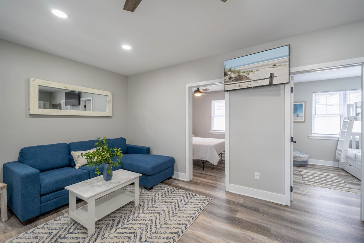 Comfortable living area with a sectional sofa, wall-mounted TV, and soft lighting. The space connects easily to the bedrooms, creating a practical layout for relaxing, watching TV, or moving between shared and private areas.