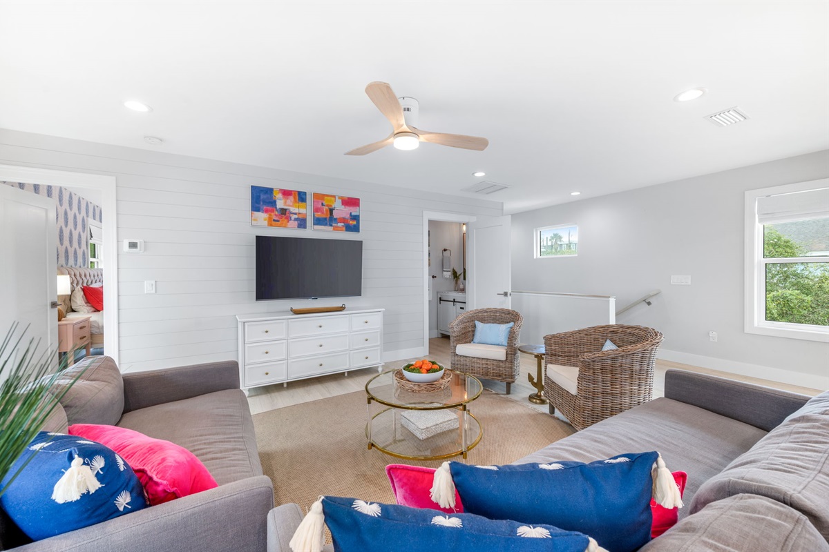 Here’s the cozy living room, perfect for winding down with friends and family after a day at the beach. The stairs to the downstairs are on the right, and the door to the upstairs master is on the left—ideal for relaxing and catching a movie together!