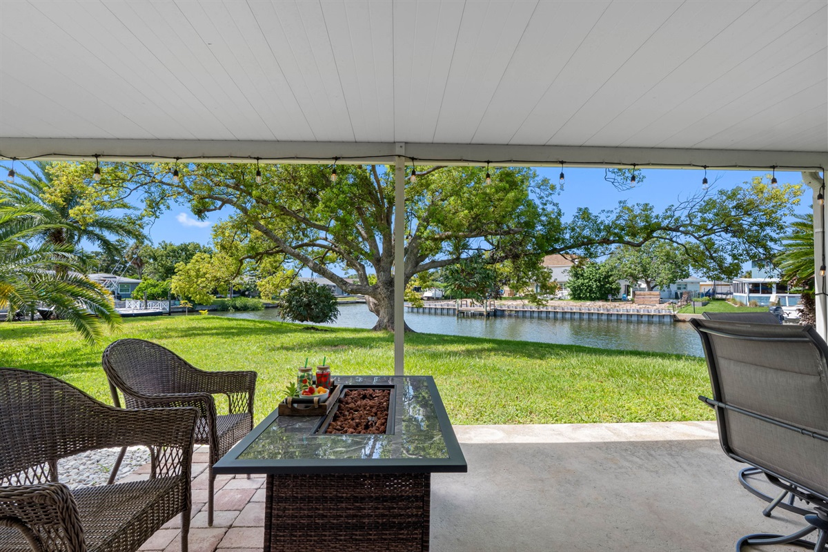 This covered patio offers a serene waterfront setting with lush greenery, perfect for relaxing by the canal and taking in the peaceful views.