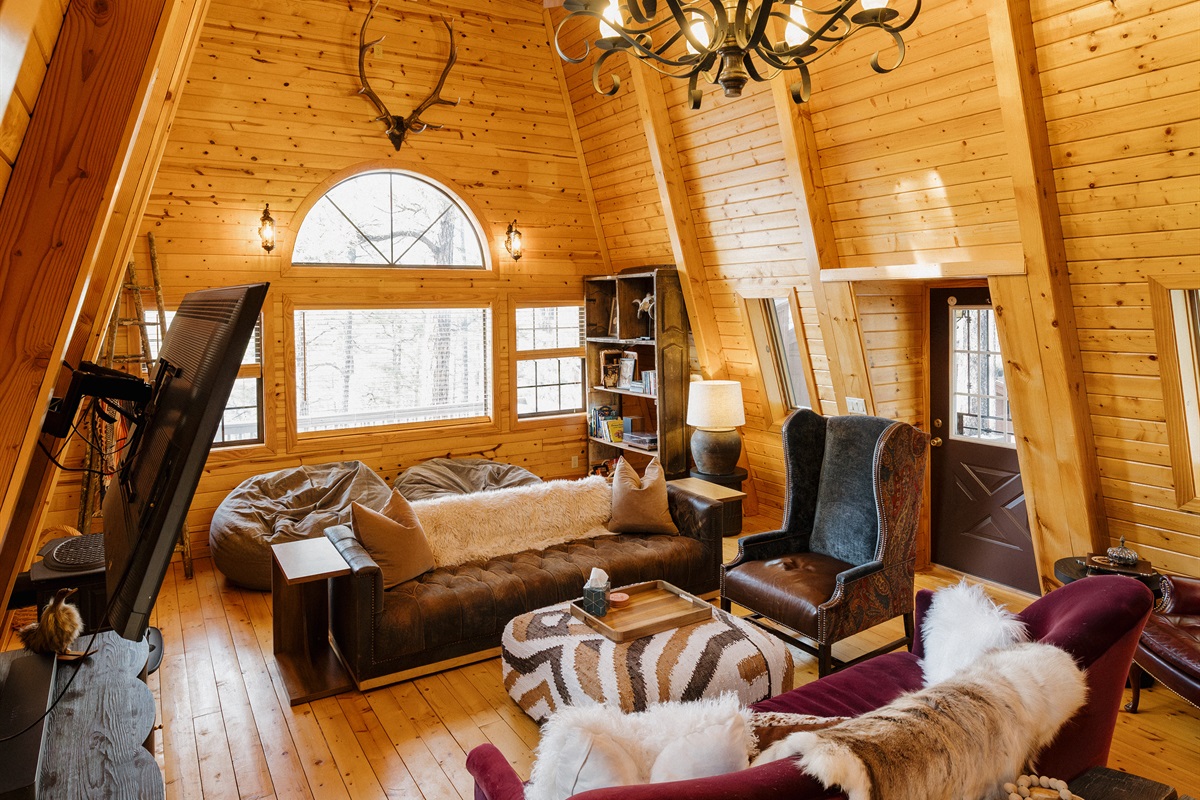 Light-filled A-frame living room with vaulted wood ceilings, eclectic seating, and cozy gathering spaces—perfect for lounging, game nights, and slow mornings in a warm, character-filled White Mountains cabin.