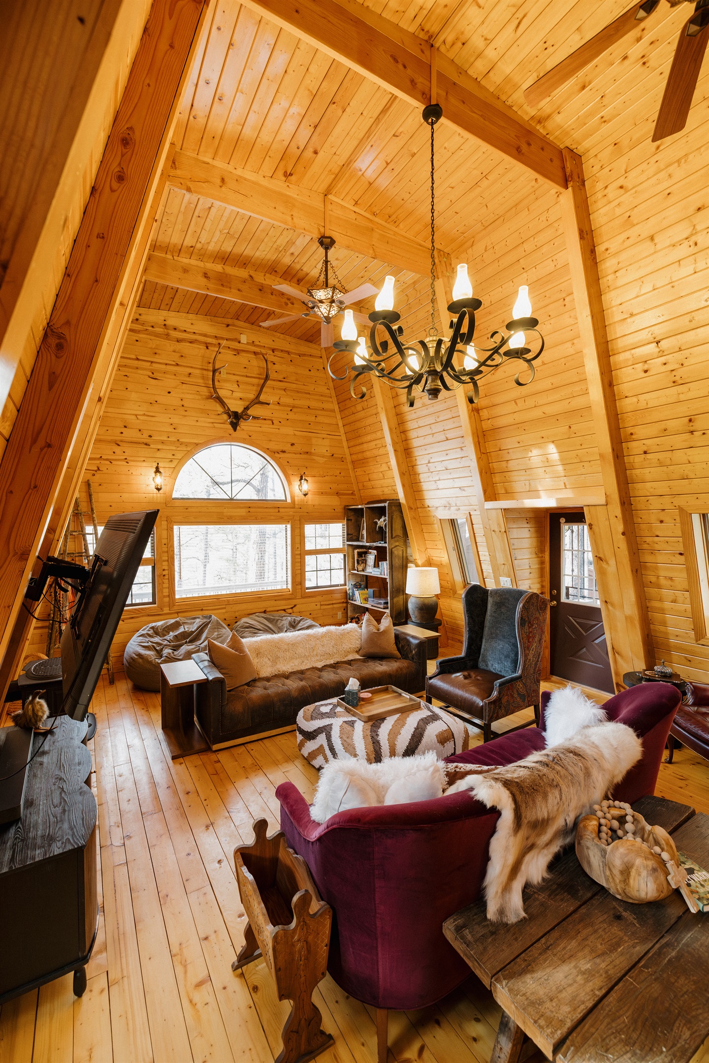 Light-filled A-frame living room with vaulted wood ceilings, eclectic seating, and cozy gathering spaces—perfect for lounging, game nights, and slow mornings in a warm, character-filled White Mountains cabin.