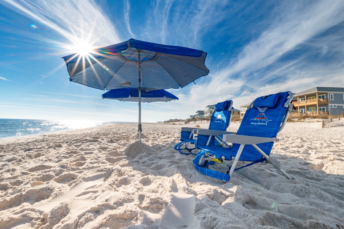 Relaxing beach escape: Blue chairs and umbrella under sunny, serene skies.