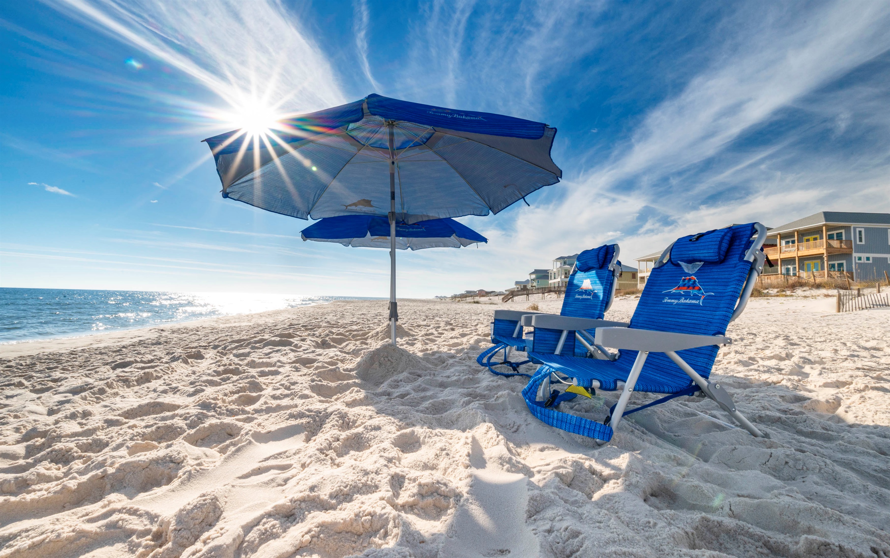 Relaxing beach escape: Blue chairs and umbrella under sunny, serene skies.