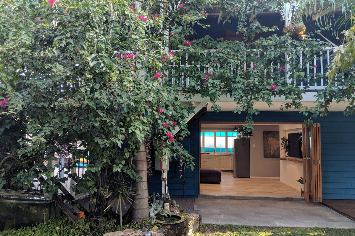 Deep blue cladding, flowering greenery and an elevated balcony give this side of Aaron's Beachside Boat House a distinctive, character-filled coastal look.
