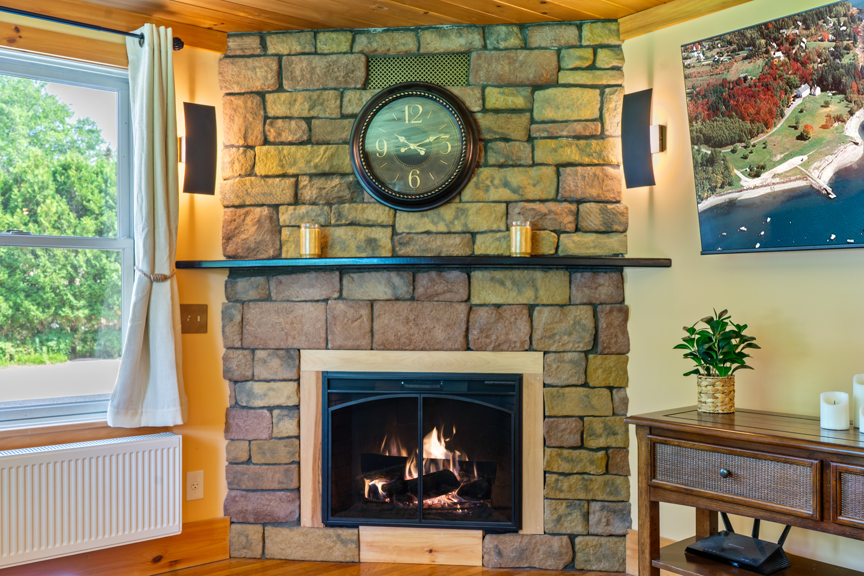 Cozy up by the warm ambient glow of the electric fireplace featured in the corner of the living room. Built with a rustic stone facade, a dark wood mantel, and stylish flanking wall sconces, this feature adds hassle-free warmth to the space.