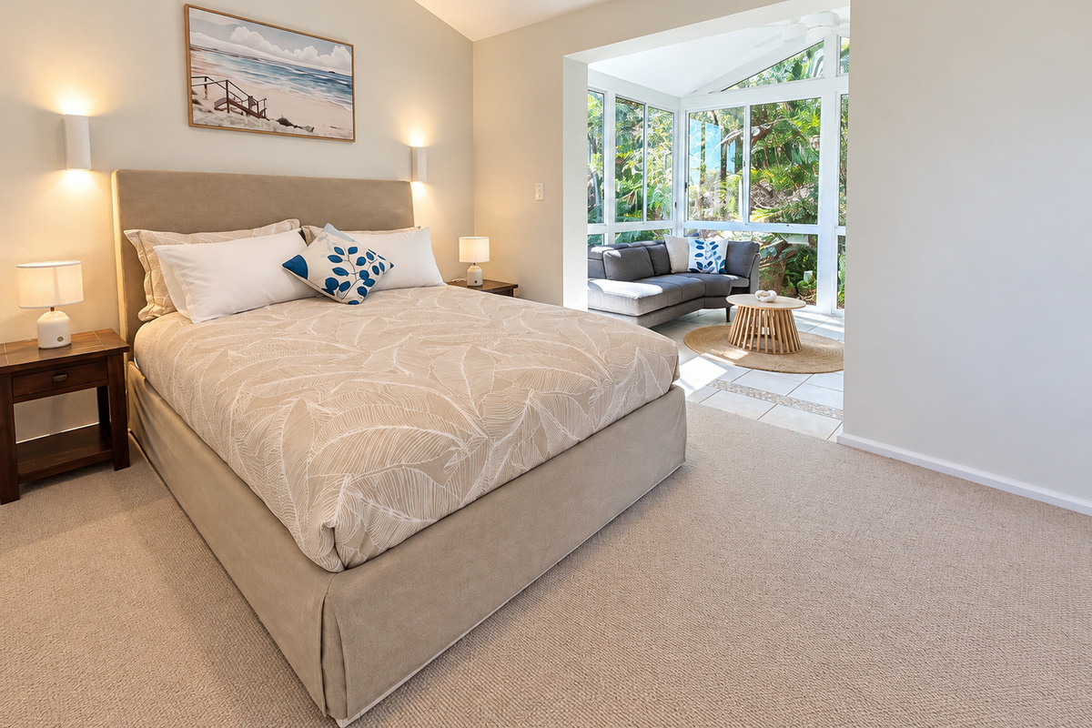 The leafy glass-wrapped sitting nook gives this Carinya Coastal Escapes bedroom a peaceful garden outlook and a bright place to unwind.