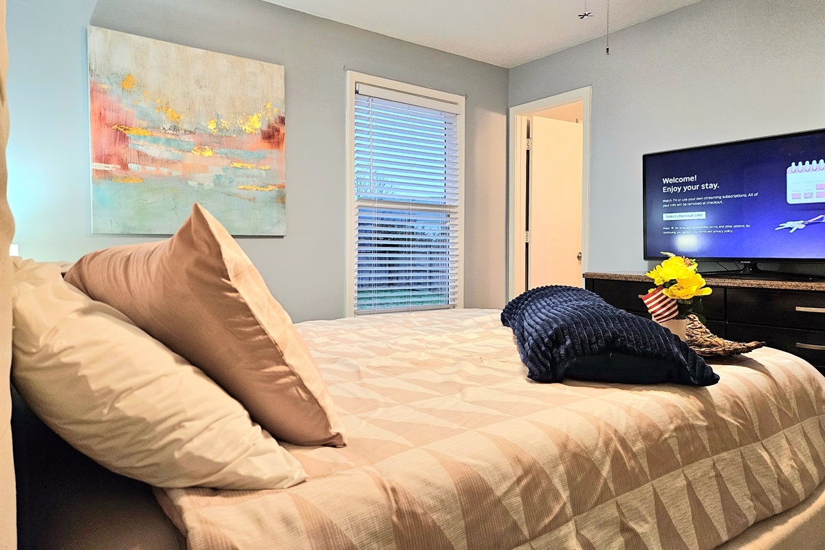 Queen primary bedroom with extra seating, ceiling fan, fast WIFI, TV, ensuite bathroom, and walk-in closet. Big window overlooking the fenced back yard adds fresh natural light and appeal.