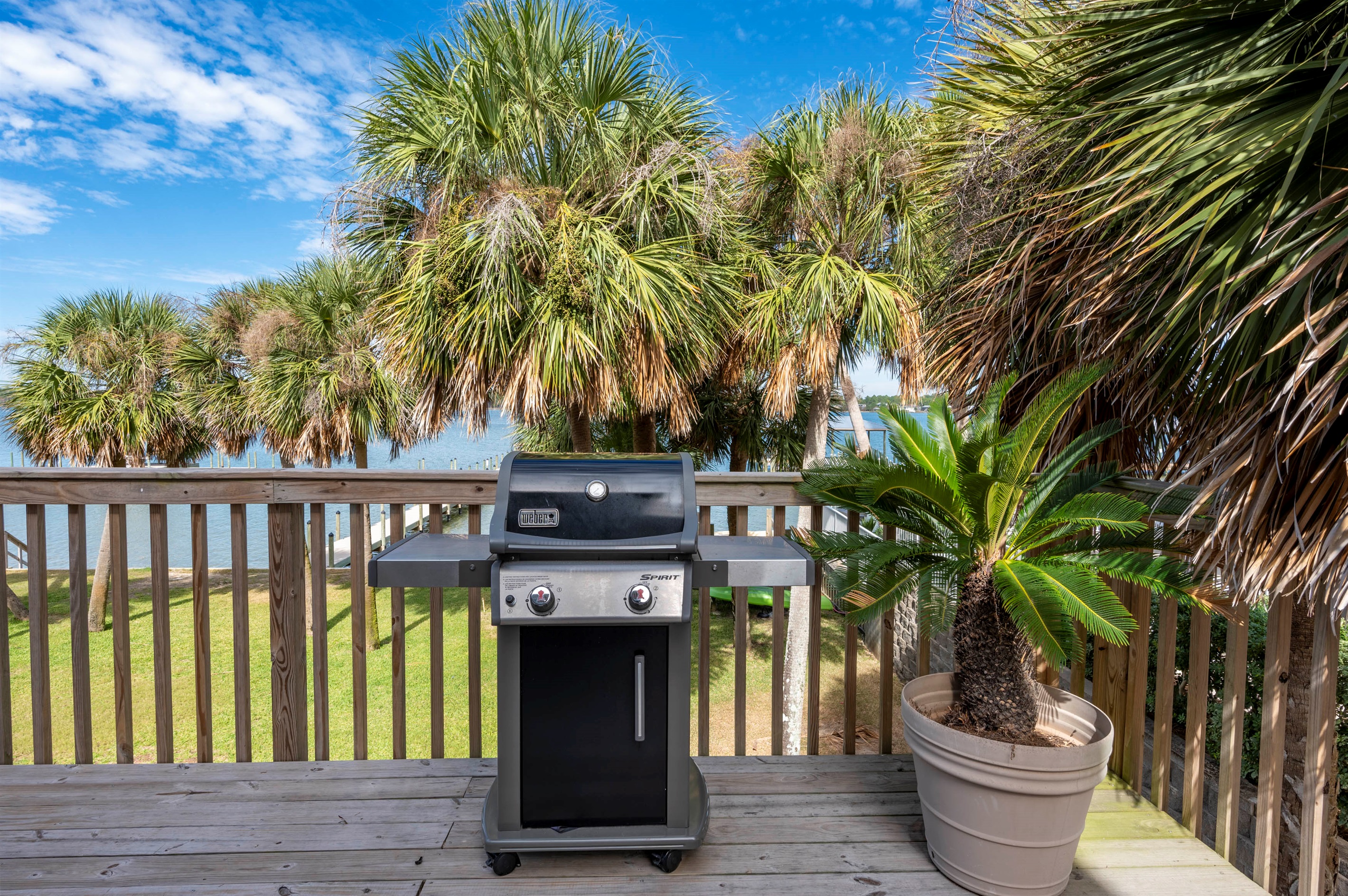 A sunny deck at “Gone Coastal” in Gulf Shores, AL, with BBQ grill, palm trees, and an ocean view for outdoor dining and relaxation.
