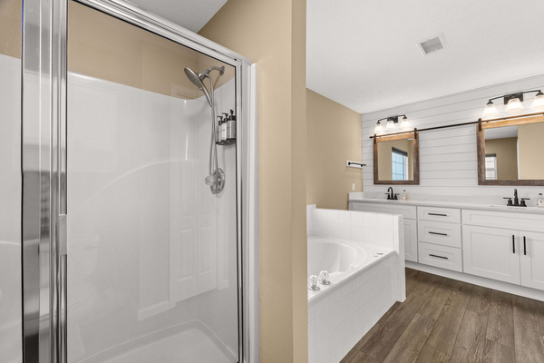 The complete master en-suite layout. In addition to the jacuzzi tub and double vanity, the private bathroom features a separate glass-door walk-in shower equipped with a modern, adjustable shower head and complimentary body care dispensers.