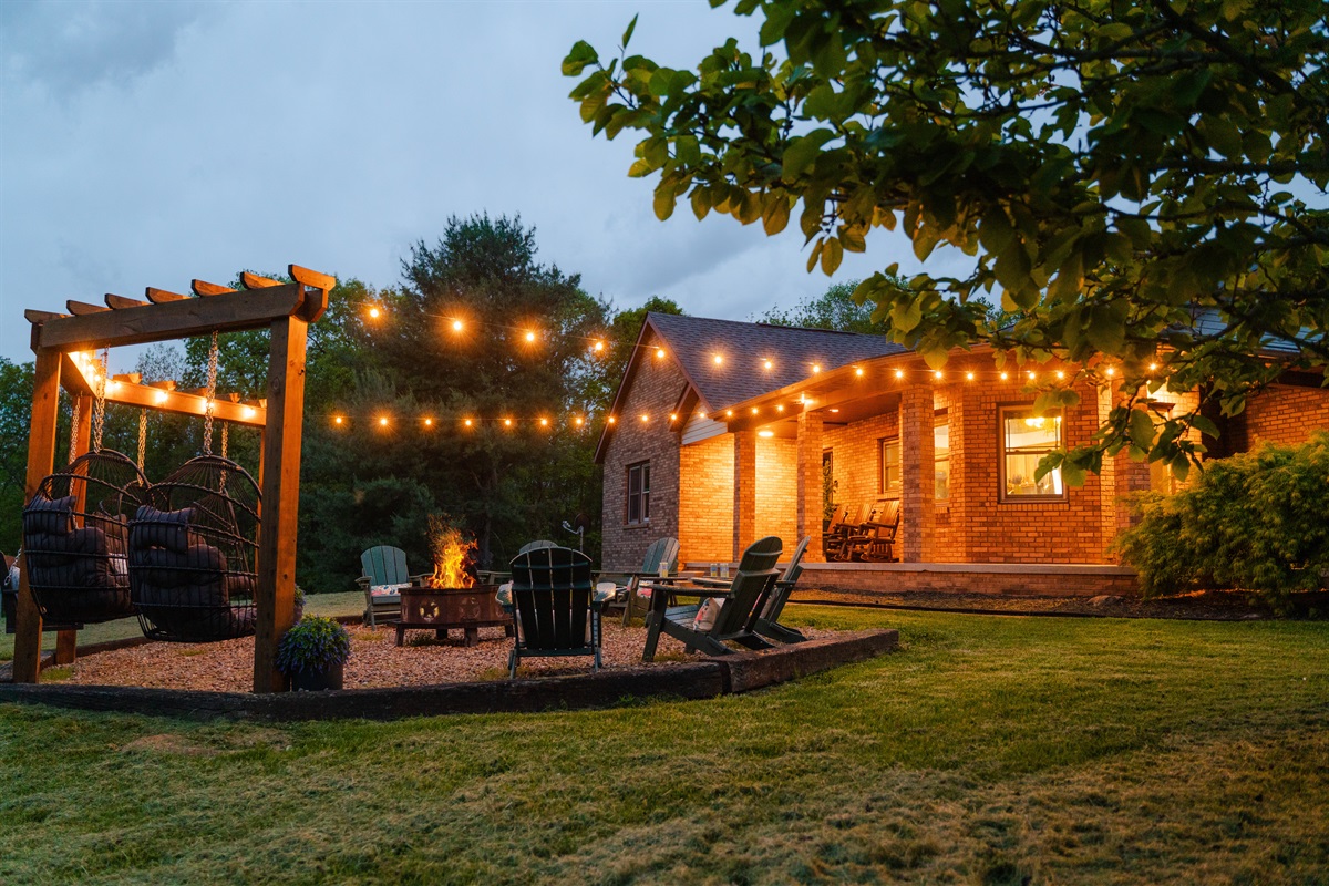 A magical outdoor setting with a firepit, swinging chairs, and string light glow