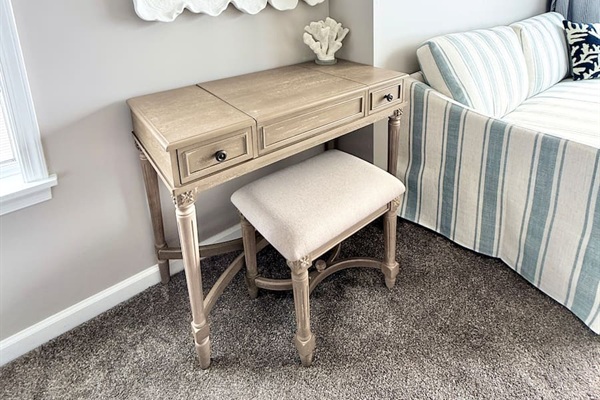 Get ready at this charming, light-toned wooden vanity paired with a matching upholstered stool, providing a stylish and functional spot for your daily routine or workstation in this cozy space.