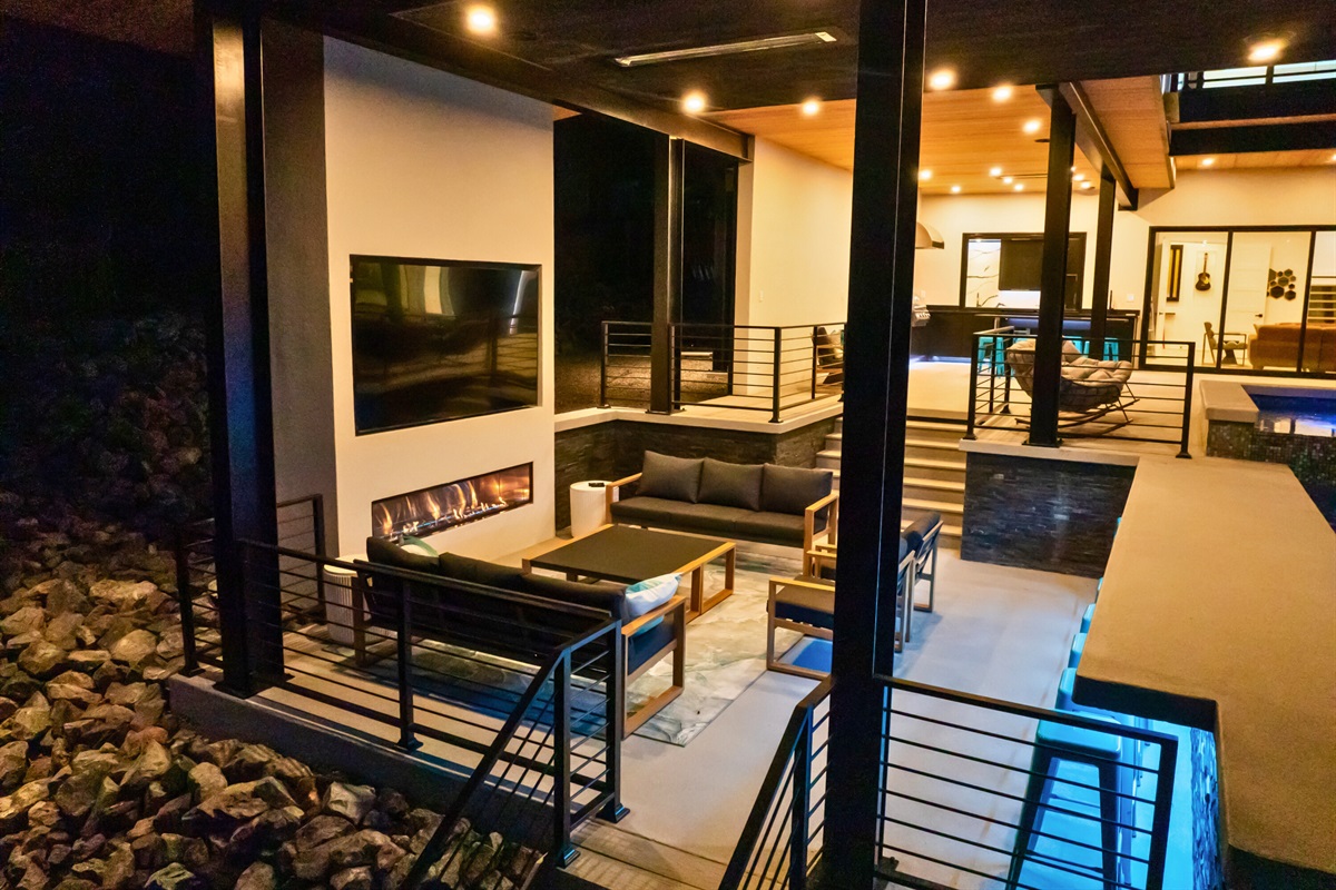 Relax in style with the outdoor living room, featuring plush seating, a TV, and a warm fireplace.