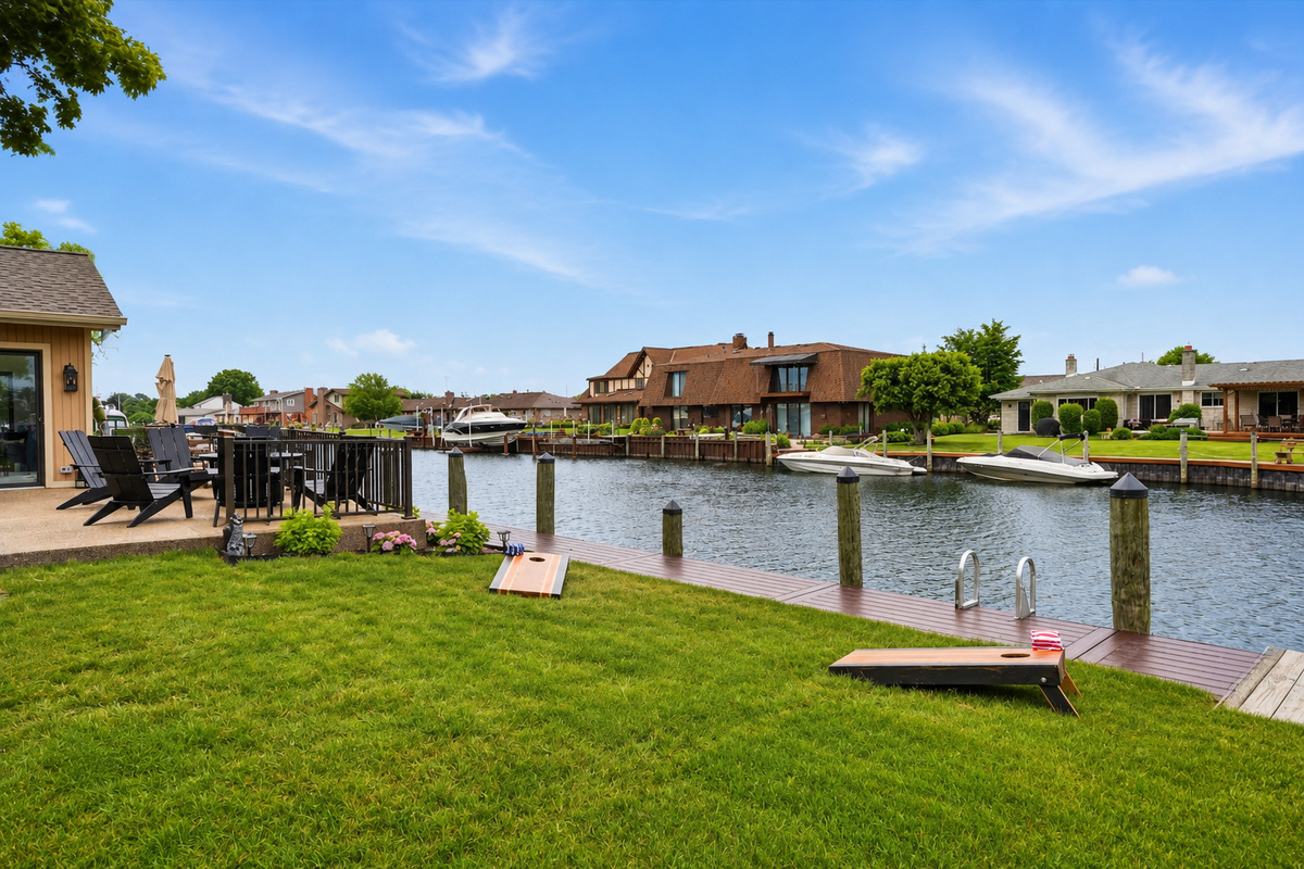 Waterfront lawn with cornhole setup and dock access, offering a peaceful outdoor space for games, relaxation, and scenic canal views.