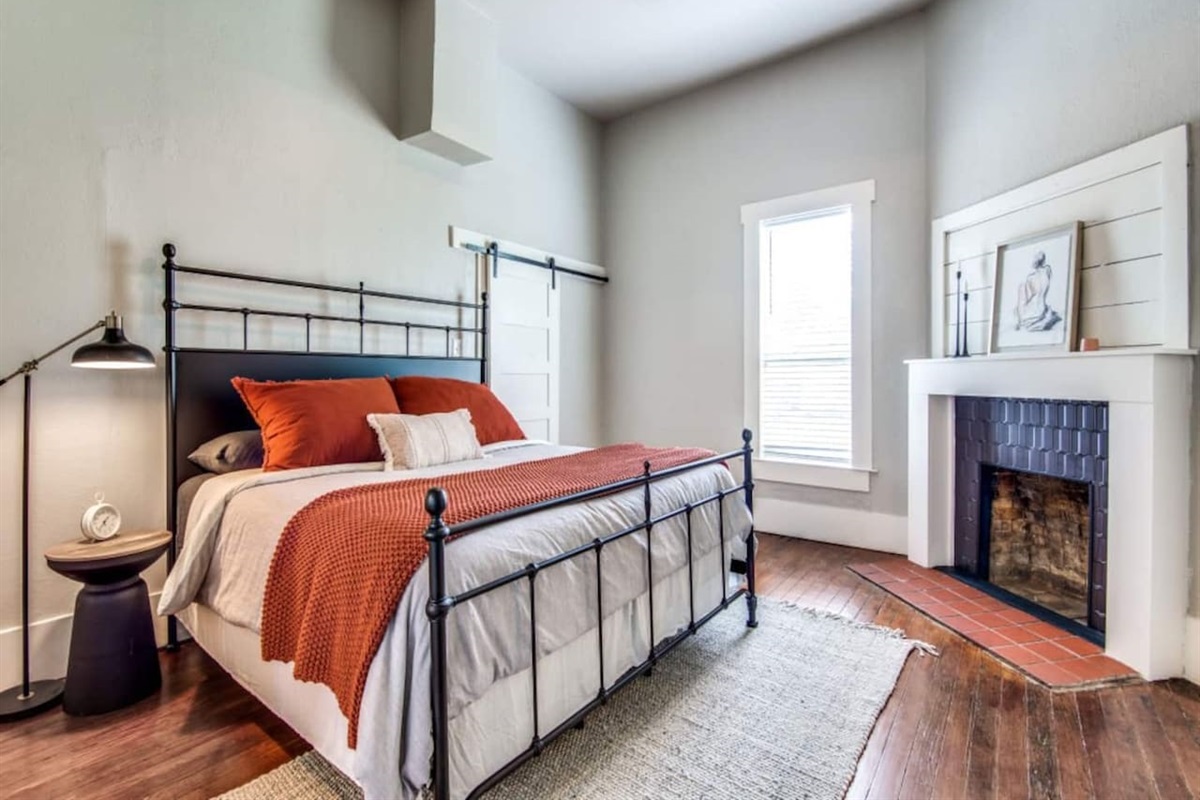 King primary suite with iron-frame bed, terracotta bedding, hardwood floors, ceiling fan, and decorative fireplace. Private ensuite bathroom included. Modern farmhouse Airbnb steps from downtown Aubrey TX near Denton County wedding venues.