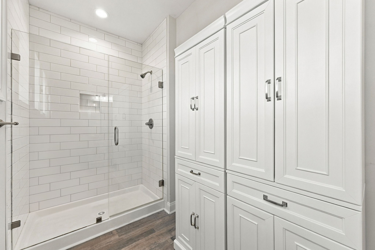 Modern ensuite bathroom featuring a glass-enclosed walk-in shower with white subway tile and custom built-in white storage cabinetry.   