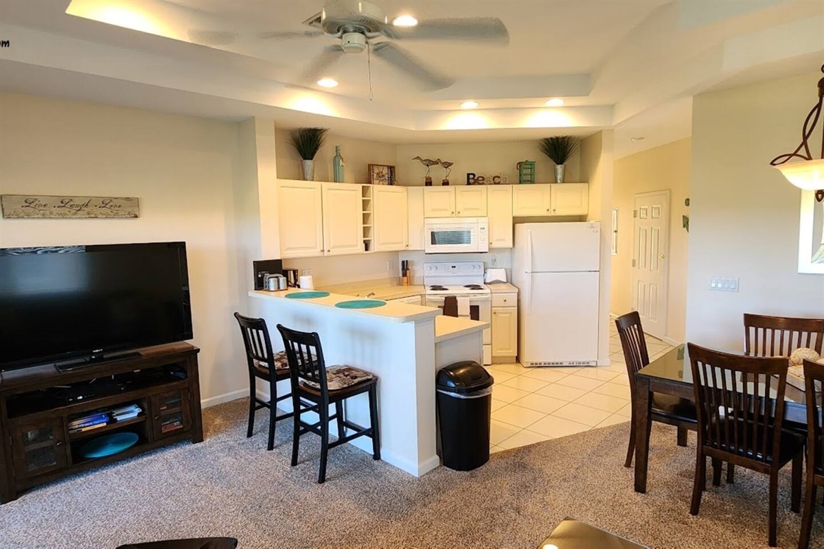 Bright kitchen and living space with breakfast bar seating, dining area, large TV, and an open layout perfect for relaxing.