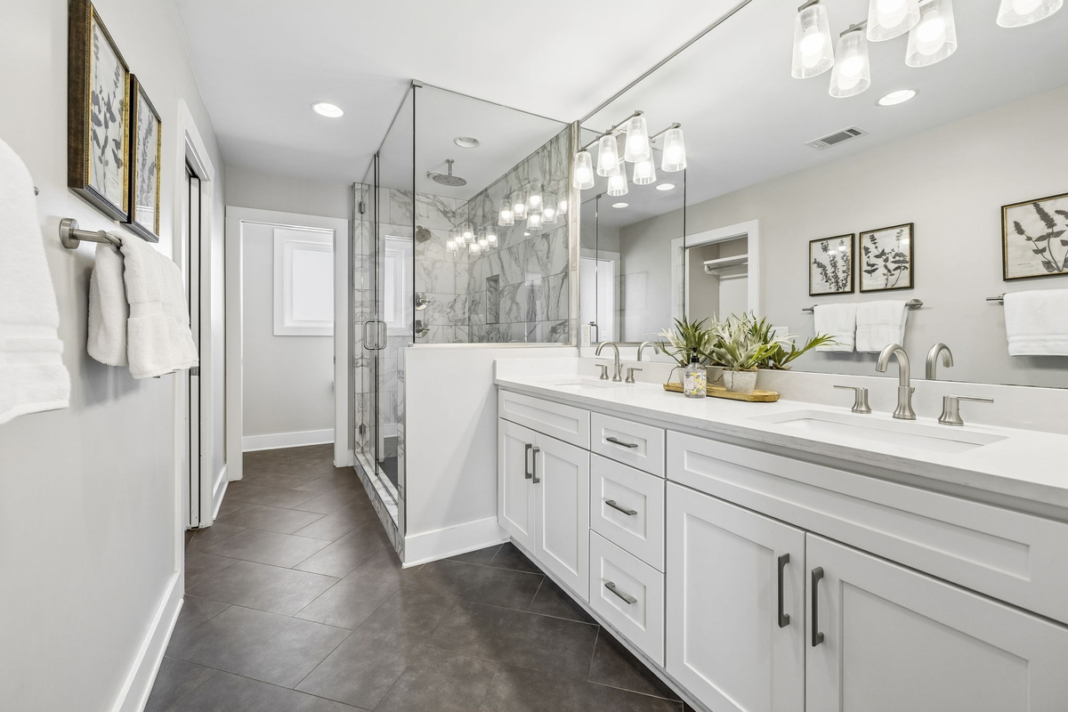 Double sink vanity with modern brushed nickel fixtures and full wall mirror design - Elegant lighting and decorative greenery bring warmth to the sleek, clean space - Glass enclosed shower and easy layout offer a spa like experience with everyday ease
