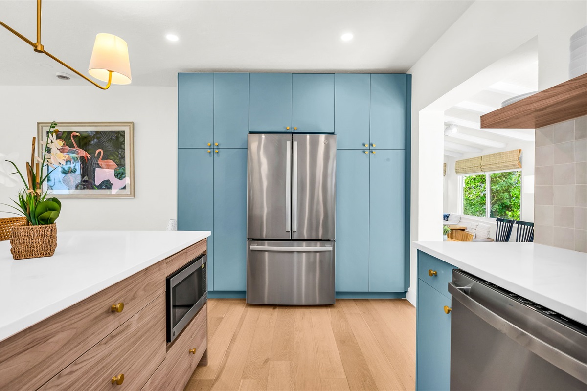 Gourmet kitchen with sleek quartz countertops, custom blue cabinetry, brass accents, and high-end stainless steel appliances. Features an oversized island with seating, open shelving, and designer lighting—perfect for both cooking and entertaining in style