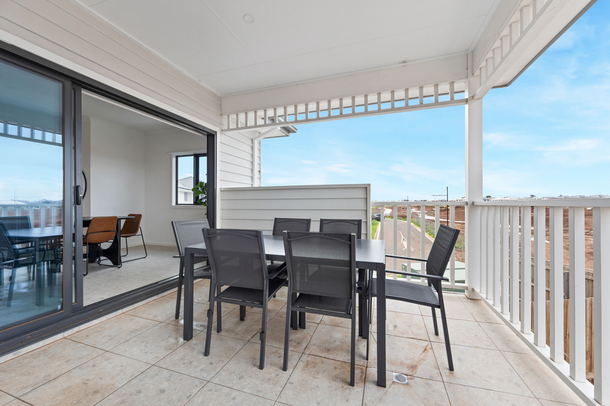 Covered upstairs balcony with an outdoor dining table and chairs, white balustrade and open views over the surrounding area.