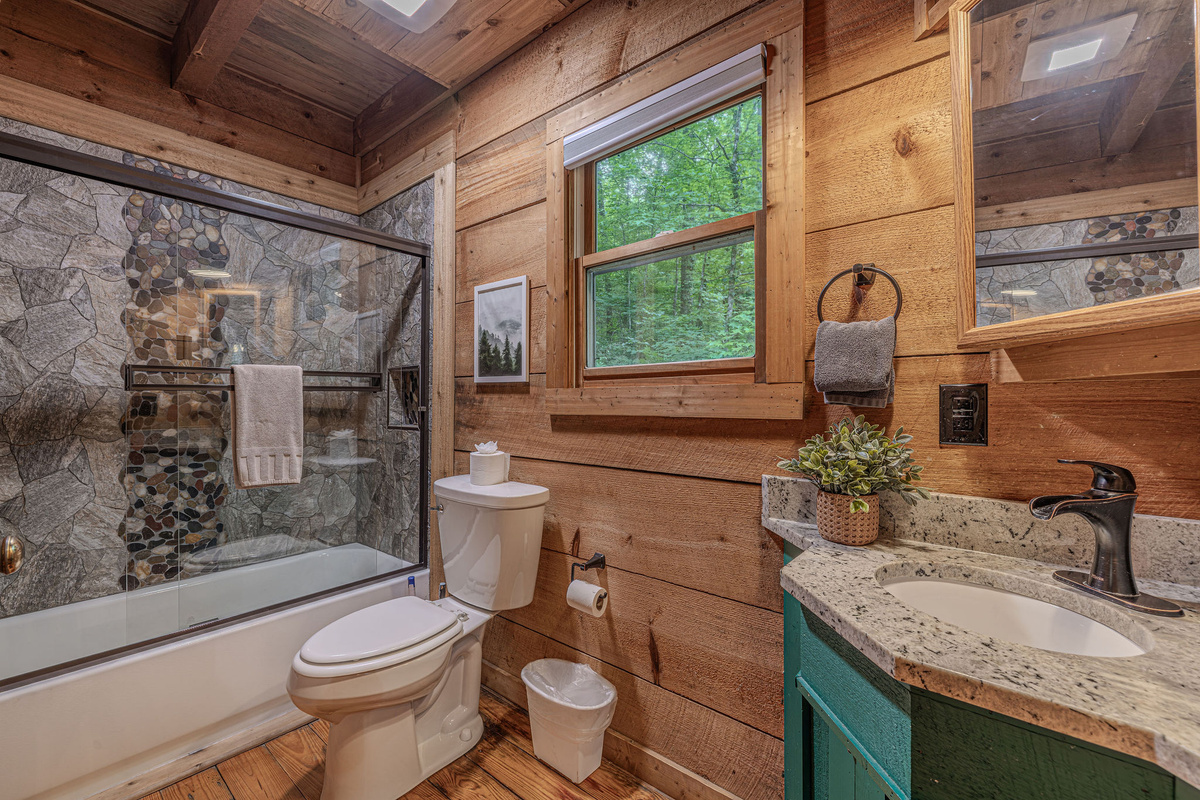 Stone tile shower, tub, and a window with tree views.