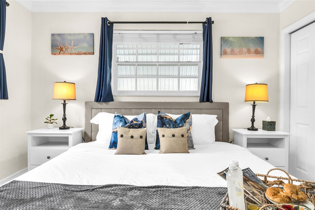 Unwind in the serene primary suite with a king bed, soft linens, and sunlit windows—your peaceful escape after a day at the beach.