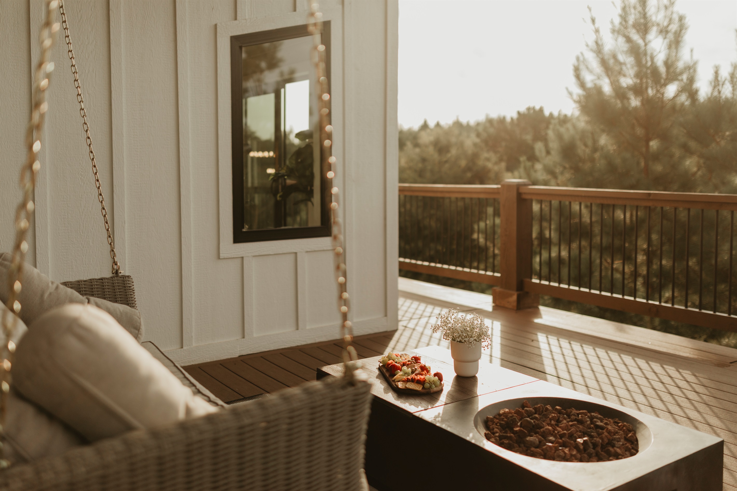 A cozy porch retreat with a swinging sofa, fire table, and peaceful forest views. Perfect for slow mornings with coffee, sunset chats, or starlit nights by the fire.