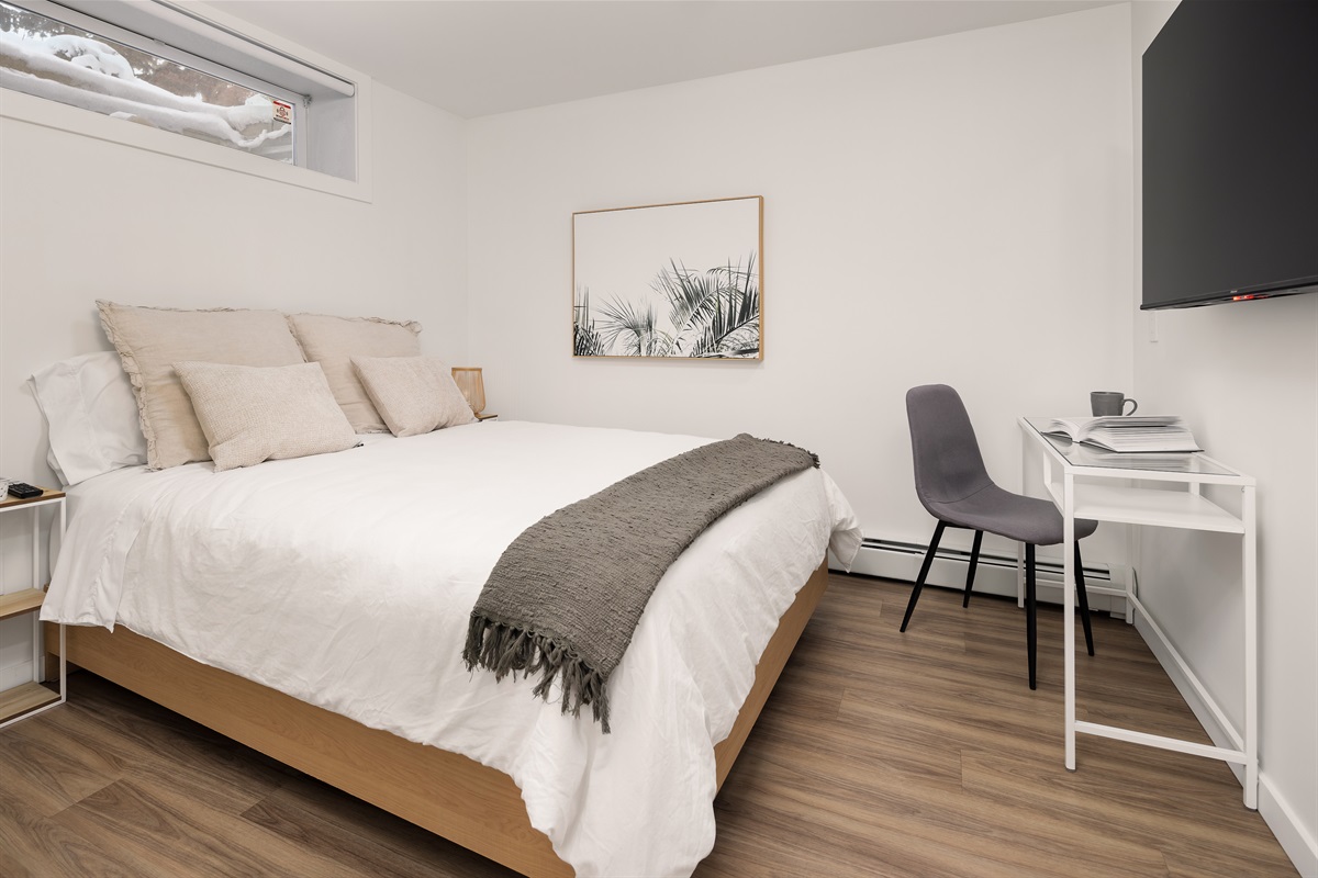 Second bedroom with queen bed, dedicated workspace, and wall-mounted Smart TV.