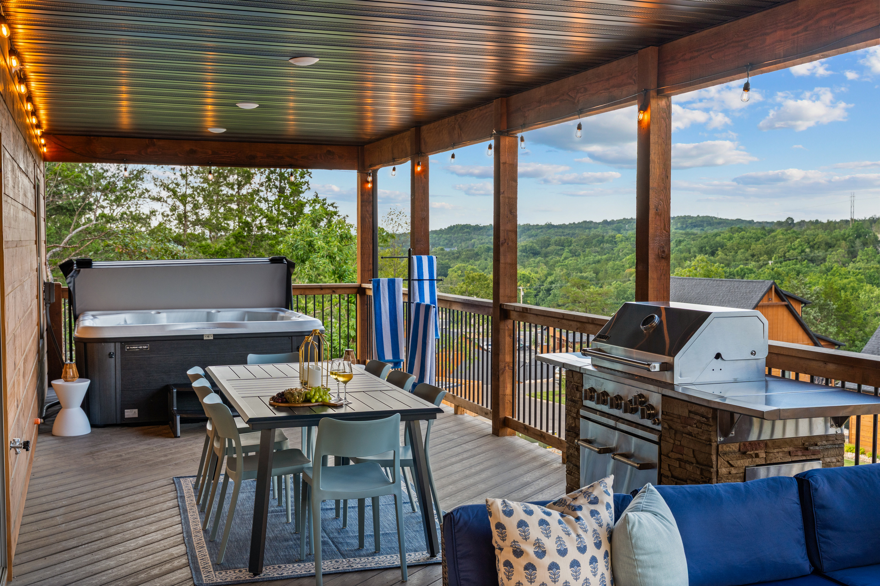 Hot tub, dining table, and a stainless gas grill all share the covered deck under the string lights.