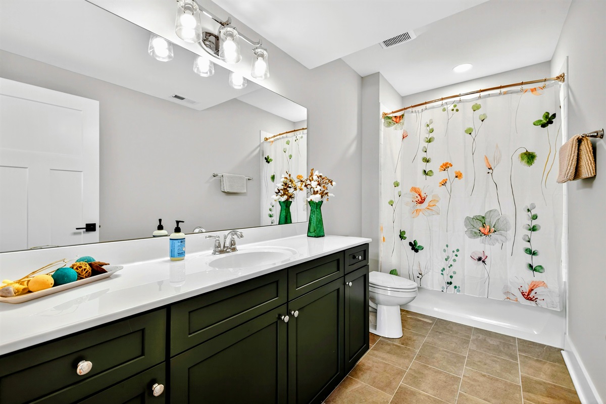 A spacious en-suite master bathroom, mirrors the serene color palette of greens and neutrals of the bedroom to offer a spa like retreat.