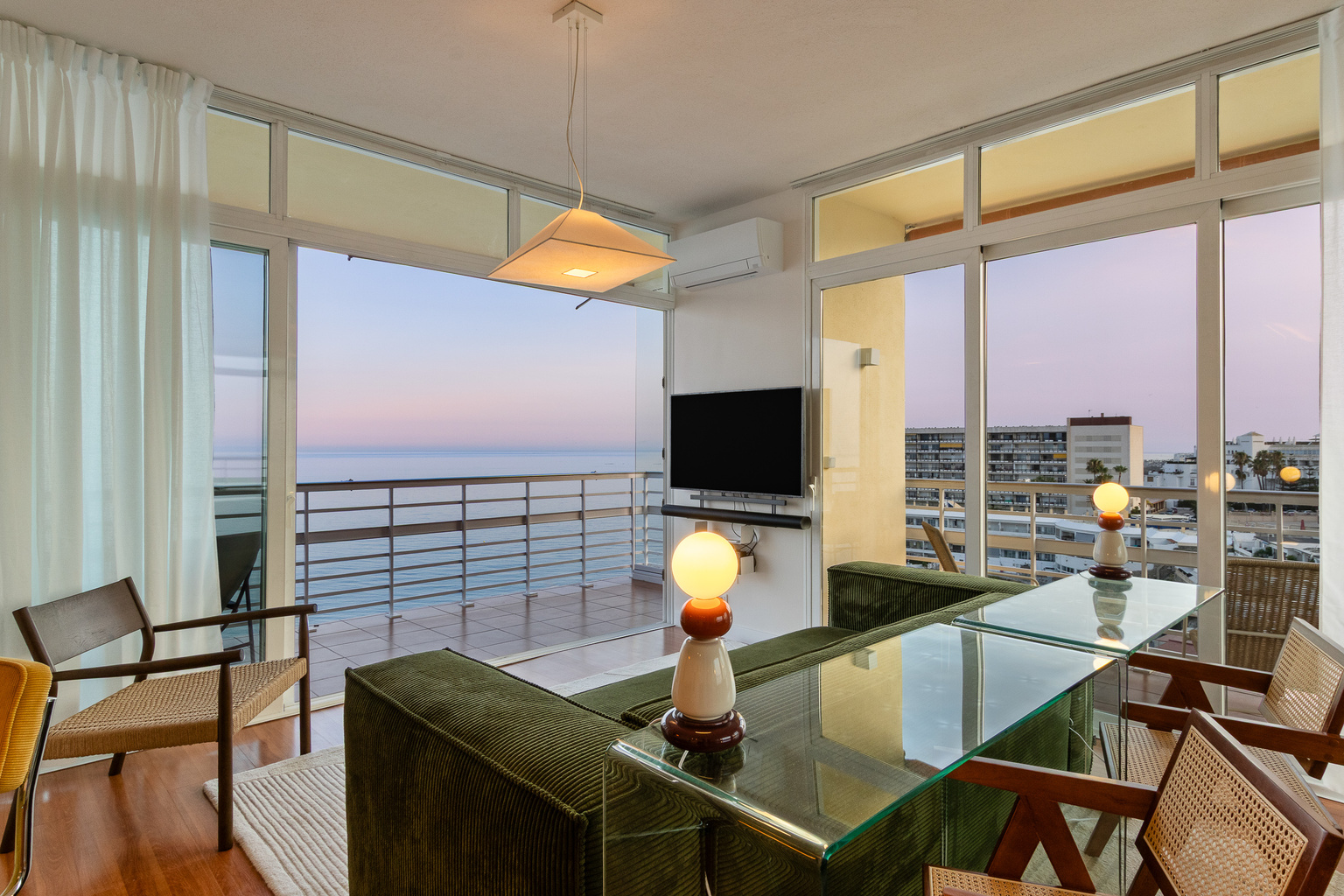Indoor-outdoor living with an open balcony, sea views and warm evening light.