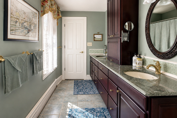 The primary en suite — double mahogany vanity, granite counters, brass fixtures, and a green glass tile backsplash. A proper bathroom for a proper Cape May summer.