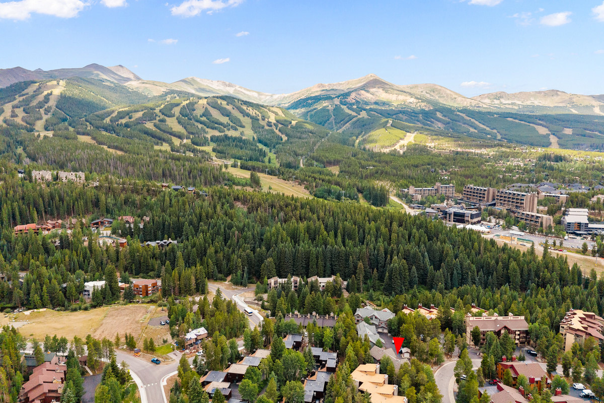 Red arrow shows aerial view of Columbine Pine Creek Retreat with summer view of Breckenridge Ski Resort in background. 