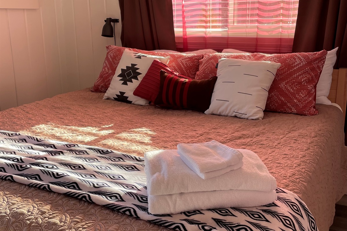 The master bedroom features a king bed with patterned textiles and layered textures throughout. Curtains, bedding, and rug create a warm, inviting, and thoughtfully styled retreat.