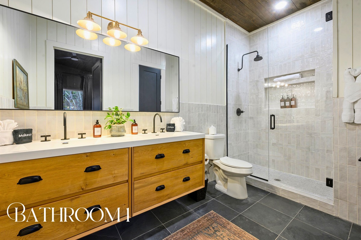 The attached bathroom offers a modern double vanity, a spacious shower, and soothing natural finishes.