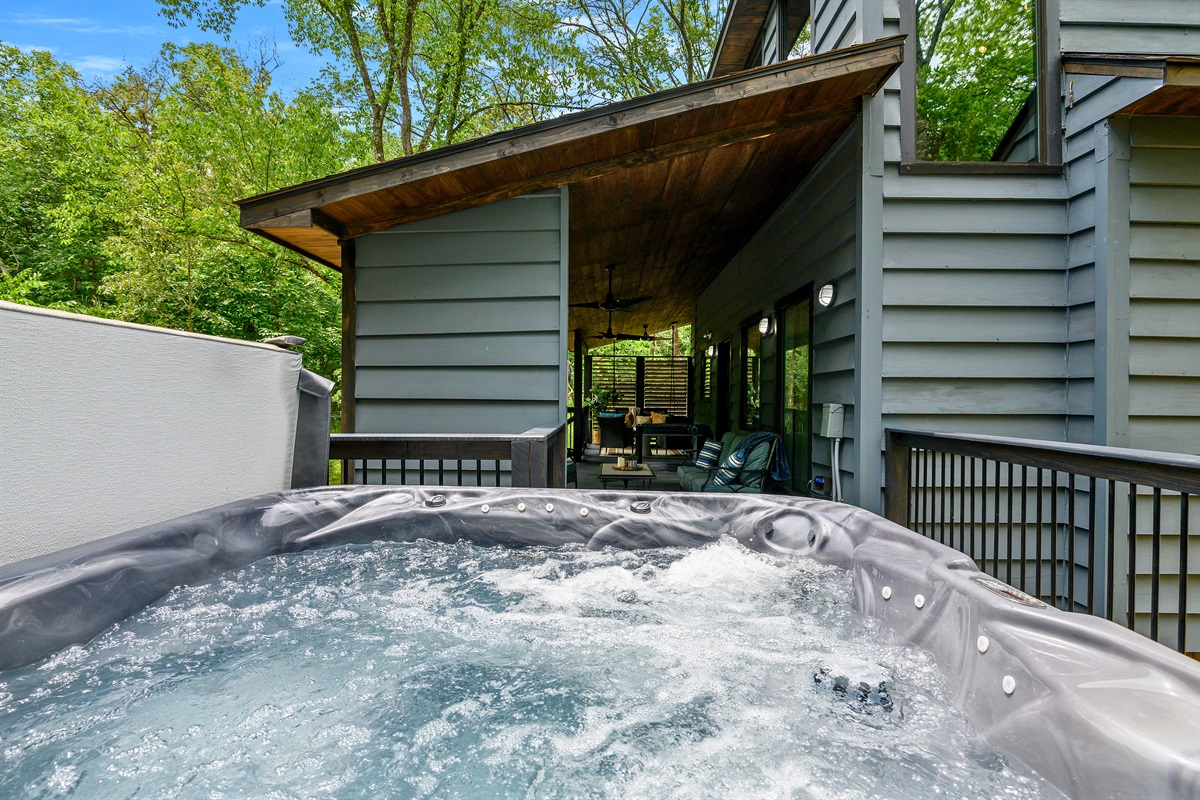 Relax in the bubbling hot tub on the covered deck, surrounded by lush greenery and modern cabin comfort.