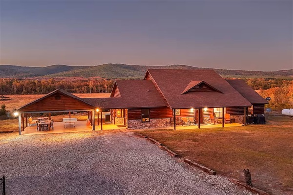 Evening exterior view of the cabin glowing against the mountain backdrop.