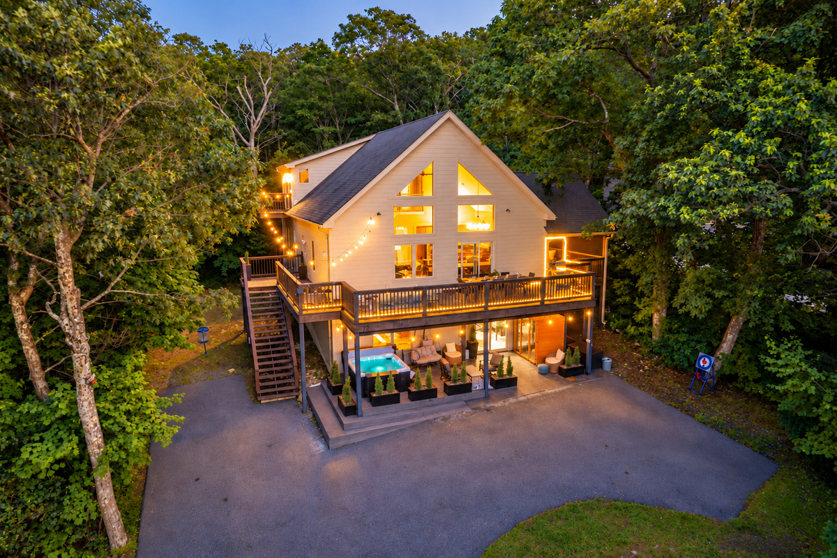 Twilight drone view showcases the home’s glowing deck lighting, multiple outdoor zones, and tree-wrapped privacy just steps from the Blue Ridge Parkway