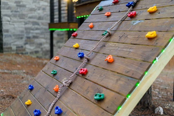 Adventure awaits with this wooden climbing wall, featuring colorful rock grips and an attached rope ladder—perfect for kids’ outdoor fun at this family-friendly cabin rental.