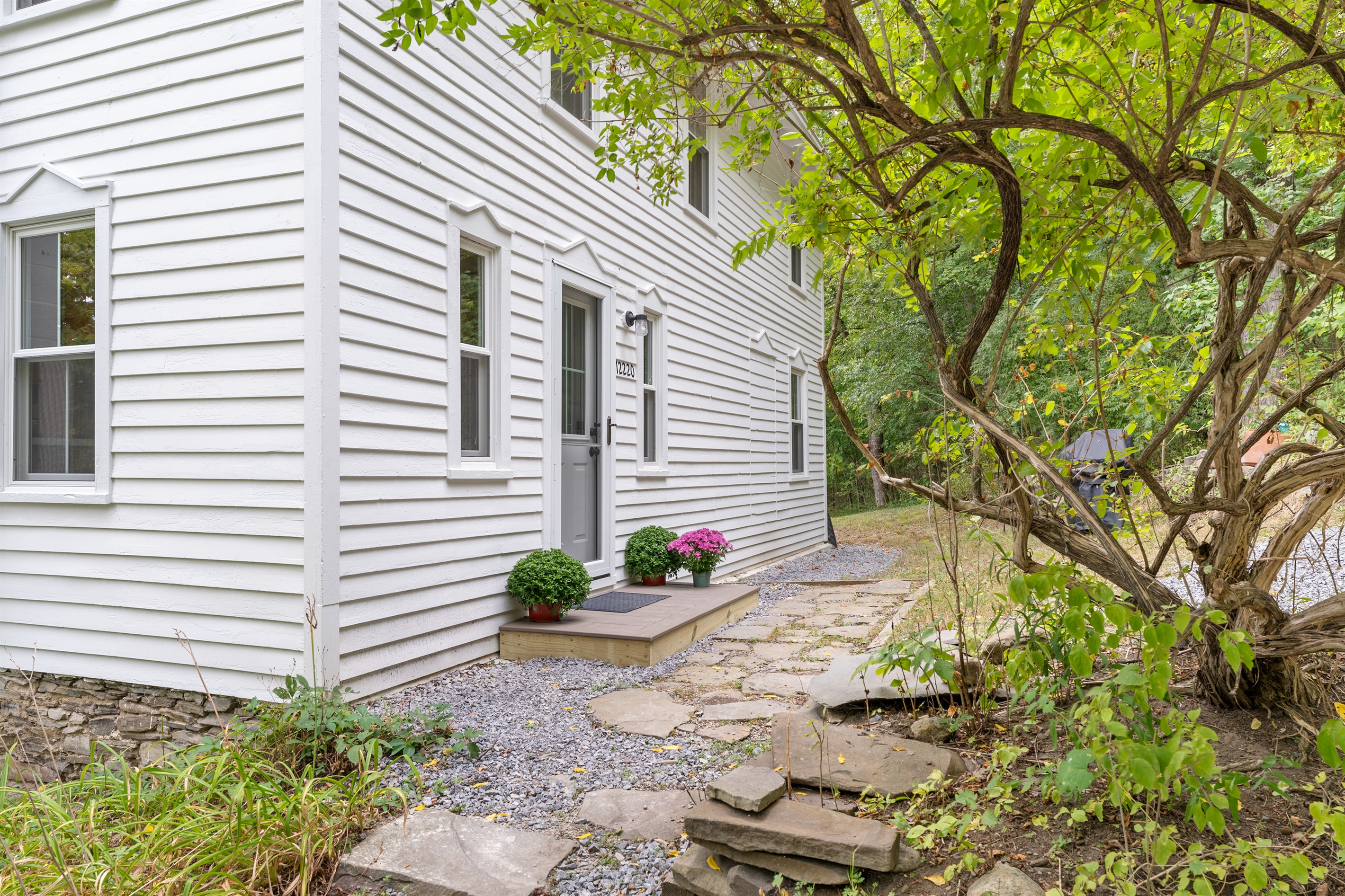 Classic white home nestled among trees with a spacious gravel driveway for easy access.