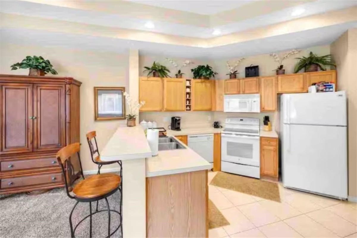 Fully equipped kitchen with cabinet storage, full-size appliances, breakfast bar seating, and an open view into the living space.
