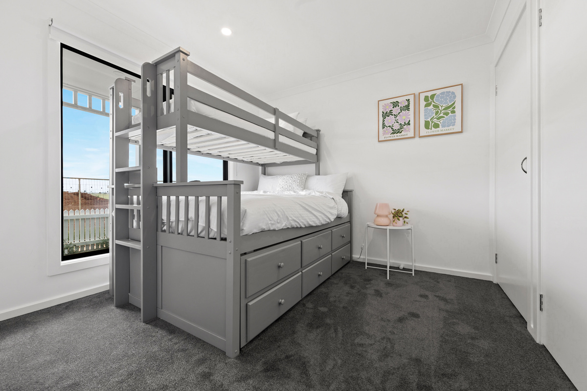 Another angle of the bunk bed, ladder and under-bed drawers, with a window letting in natural light and a small side table.