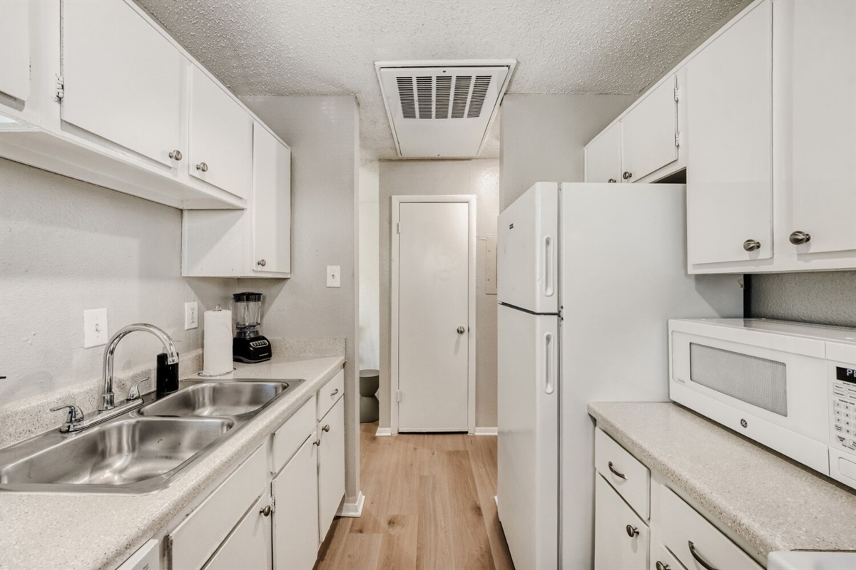 Bright galley kitchen with white cabinetry, modern appliances, and wood-style flooring.