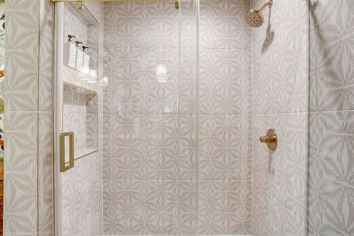 Rear bath shower with playful tile, built-in niches stocked with shampoo, conditioner, and body wash, and a sleek glass barn door finished in warm gold hardware.